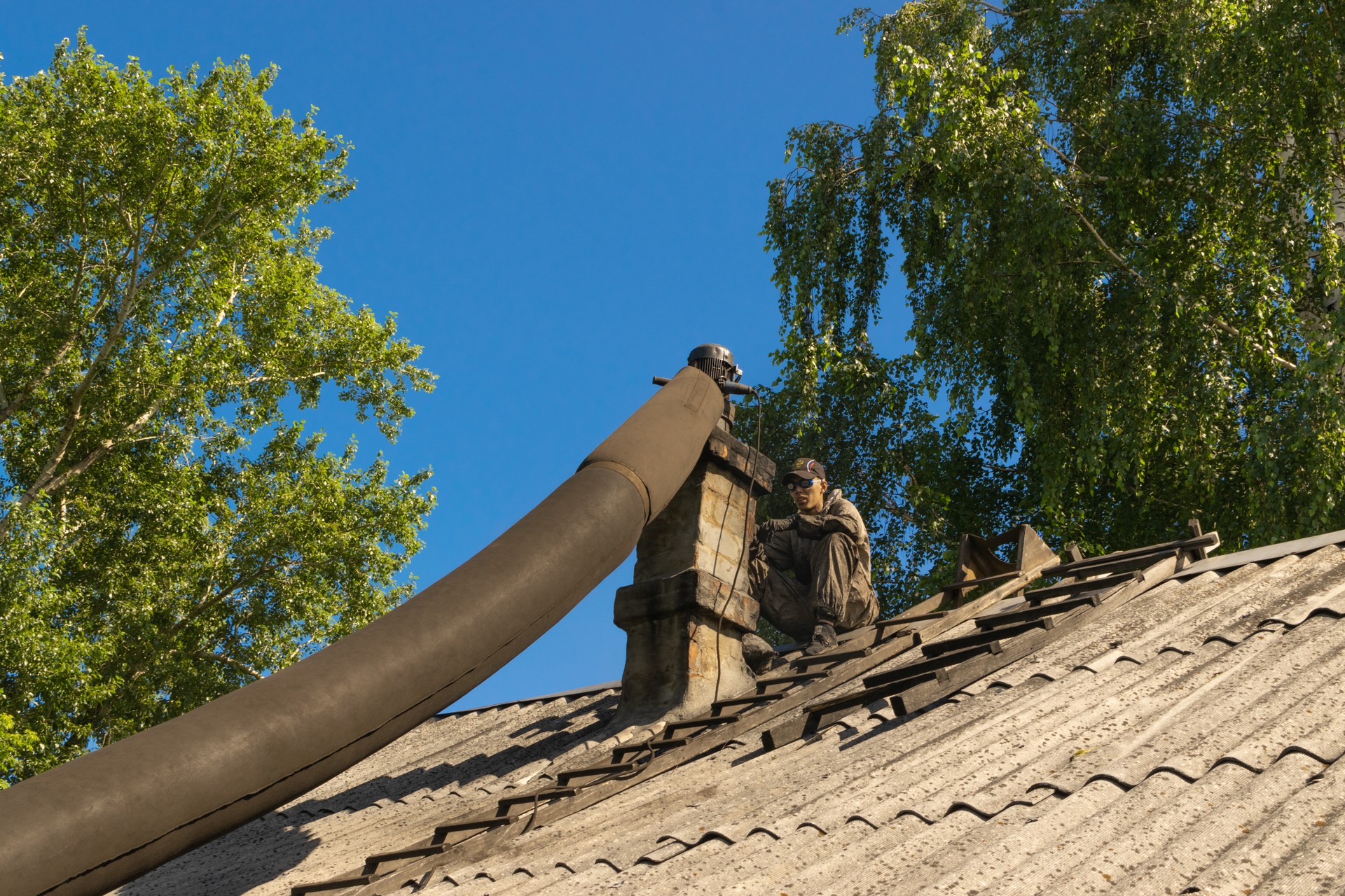 Chimney sweep man cleaning brick chimney on old building roof